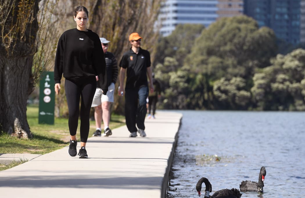 A woman passes a swan while exercising in Melbourne on September 16, 2021, as the state government announced a loosening of Covid-19 restrictions.