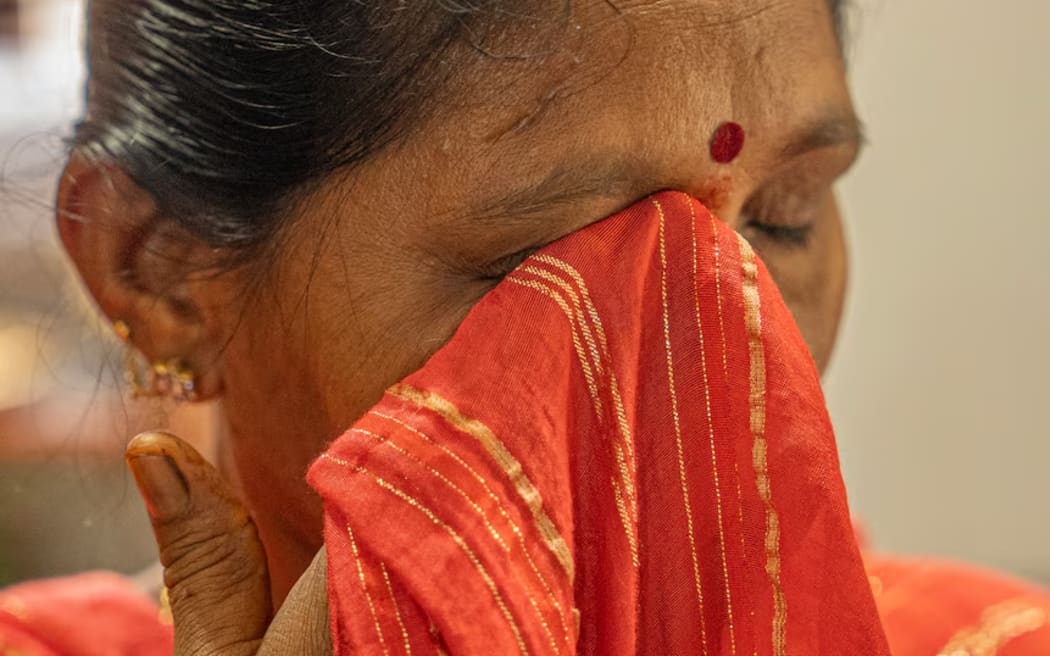 An Indian woman with her eyes closed, crying into a bright red and yellow striped saree.