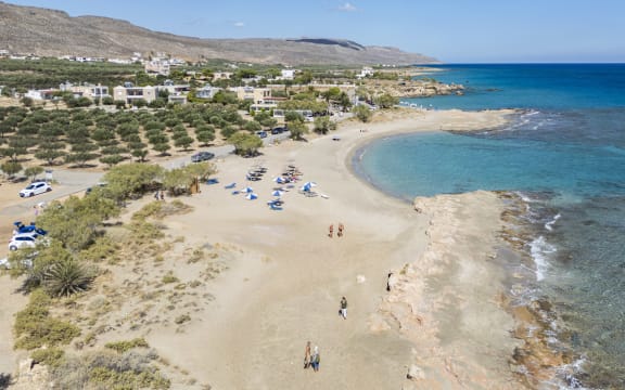 Aerial panoramic view from a drone of Xerokampos sandy beach with tourists and umbrellas next to an olive grove.  An olive grove is an agricultural olive plantation, a cultivated area of olive trees grown for fruit or oil, characterized by a geometric planting layout. The trees are typically planted in a structured, geometric arrangement to optimize space for cultivation and harvesting with the primary purpose to produce olives, which are then used for making olive oil or are consumed as table olives. Creta island in the Mediterranean sea is famous for the high quality olive oil production, while Greece is one of the global producer and largest exporters along with Spain and Italy. Xerokampos, Crete island, Greece on October 7, 2025 (Photo by Nicolas Economou/NurPhoto) (Photo by Nicolas Economou / NurPhoto via AFP)
