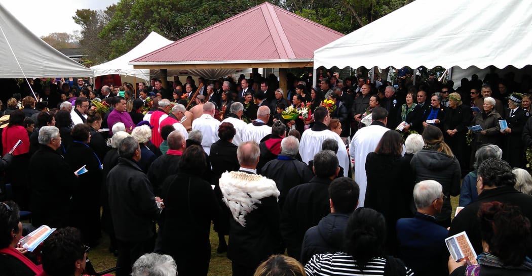 Mourners stand as the casket is taken from the marae.