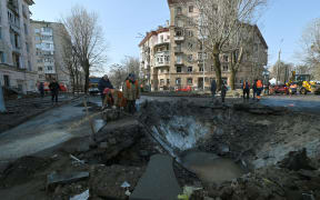 Municipal services workers survey and repair the damage following a missile attack in Kyiv, on 21 March, amid the Russian invasion of Ukraine. (Photo by Sergei CHUZAVKOV / AFP)