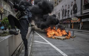 A protester jumps over a barrier after setting a fire on a road during a pro-democracy march in the Kowloon district in Hong Kong on October 20, 2019
