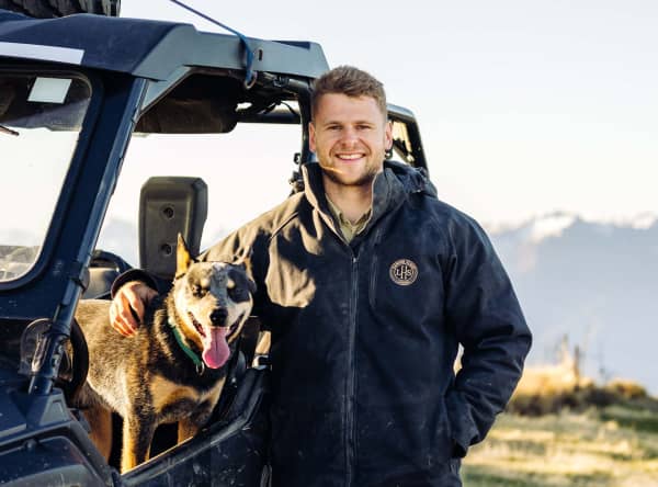 Richie Lamming is a smiling man in a thick jacket standing next to a truck with his arm around a dog.