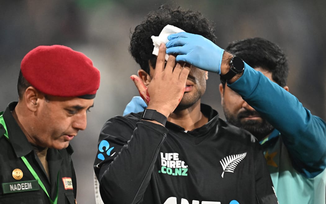 New Zealand's Rachin Ravindra (C) receives medical attention after being hit on the head by the ball during the Tri-Nation's first one-day international cricket match between Pakistan and New Zealand at the Gaddafi Stadium in Lahore on February 8, 2025.  (Photo by Farooq NAEEM / AFP)