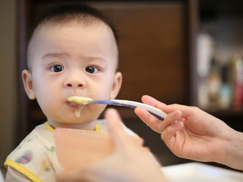 An Asian baby is fed some yellow food.