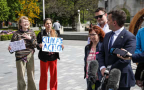 ACT leader David Seymour speaks to media with two teenage protesters standing behind him on 10 October, 2023