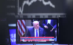 US President Donald Trump is seen on a TV screen below a display showing the German Stock Market Index DAX at the stock exchange in Frankfurt, Germany, on April 3, 2025. (Photo by Daniel ROLAND / AFP)