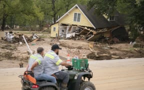 OLD FORT, NORTH CAROLINA - SEPTEMBER 30: Men on a four wheeler pass a storm damaged house along Mill Creek in the aftermath of Hurricane Helene on September 30, 2024 in Old Fort, North Carolina. According to reports, at least 90 people have been killed across the southeastern U.S., and millions are without power due to the storm, which made landfall as a Category 4 hurricane on Thursday. The White House has approved disaster declarations in North Carolina, Florida, South Carolina, Tennessee, Georgia, Virginia and Alabama, freeing up federal emergency management money and resources for those states.   Sean Rayford/Getty Images/AFP (Photo by Sean Rayford / GETTY IMAGES NORTH AMERICA / Getty Images via AFP)