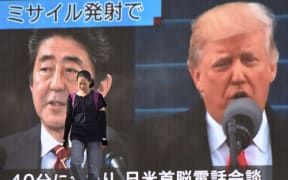 A woman walks in front of a huge screen displaying Japanese Prime Minister Shinzo Abe (L) and US President Donald Trump (R) in Tokyo.