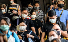 People wearing protective facemasks leave the city commuter train station in Bangkok.