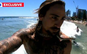 A screenshot of a 9News piece about Gold Coast man Higor Fiuza surfing with his bredli carpet python Shiva around his neck.