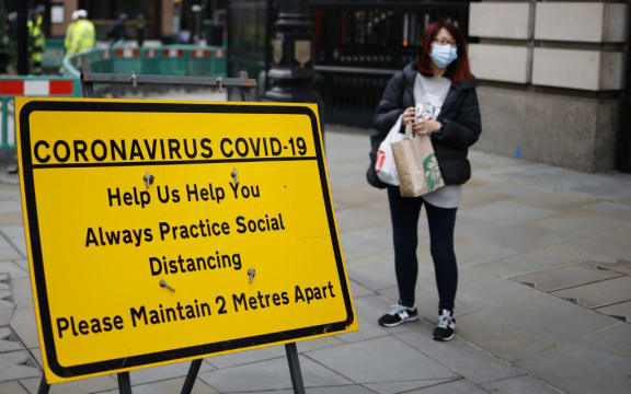A shopper wearing a facemask stands near a sign promoting social distancing in Haymarket, central London on January 8, 2021, as England entered a third lockdown due to the novel coronavirus Covid-19.