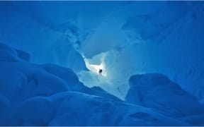 Imax Crevasse on Ross Island in Antarctica. Very blue ice cave. Climber silhouetted in Imax Crevasse in Antartica.