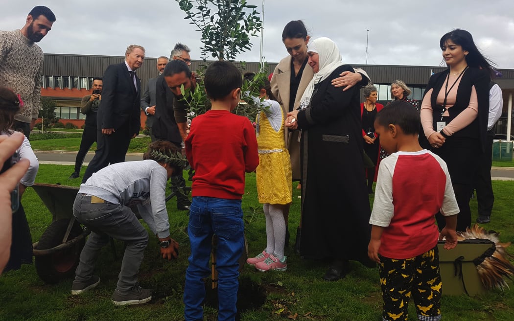 Prime Minister Jacinda Ardern plants a pōhutukawa tree in memory of the Christchurch terror attack victims, with members of one of the families, refugees who are being resettled in New Zealand.