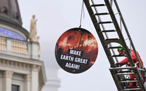 A Greenpeace environmental activist installs a round placard reading "Make the world great again" with landmark TV tower in the background in front of Germany's Foreign Ministry where the Petersberg Climate Dialogue (PCD) conference is held, on March 26, 2025. (Photo by RALF HIRSCHBERGER / AFP)