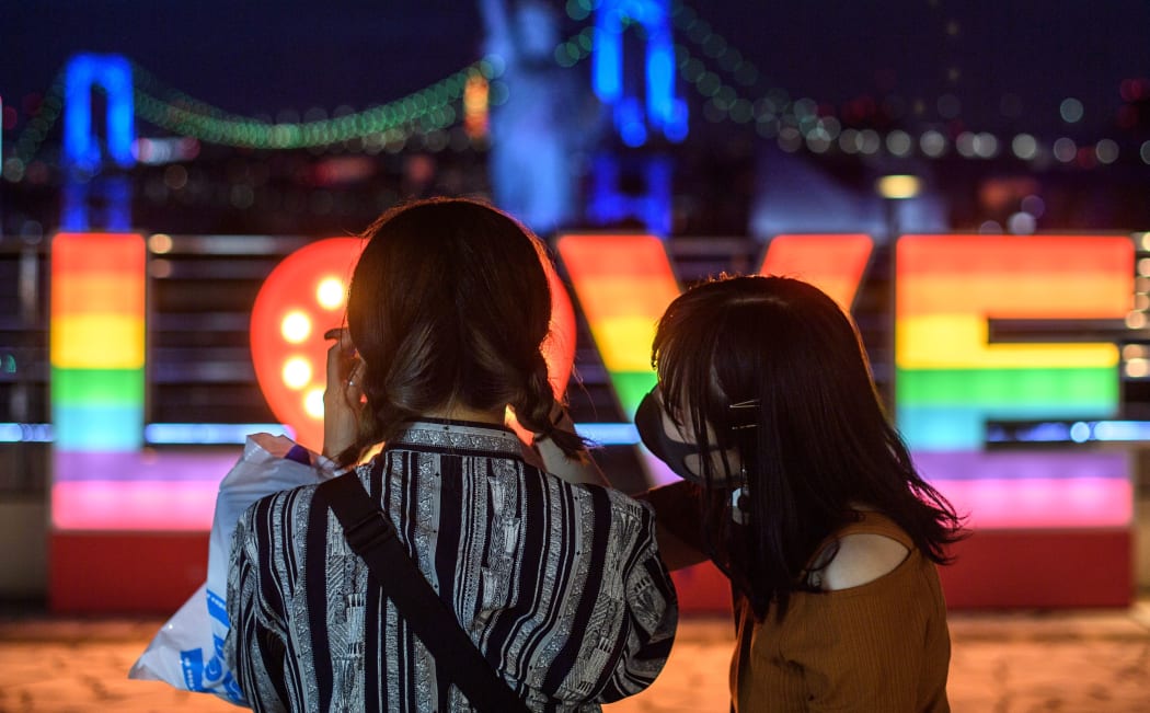 People wearing face masks take pictures at Odaiba area of Tokyo during the evening hour on July 12, 2020. (Photo by Philip FONG / AFP)