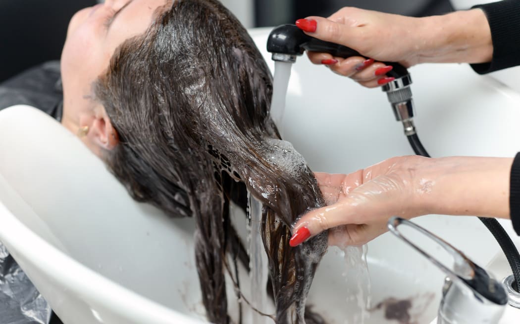 Hairdresser washing hair of a woman in a beauty salon. Water restrictions affecting businesses.