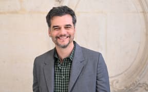 Wagner Moura is a smiling bearded man in a grey suit jacket.