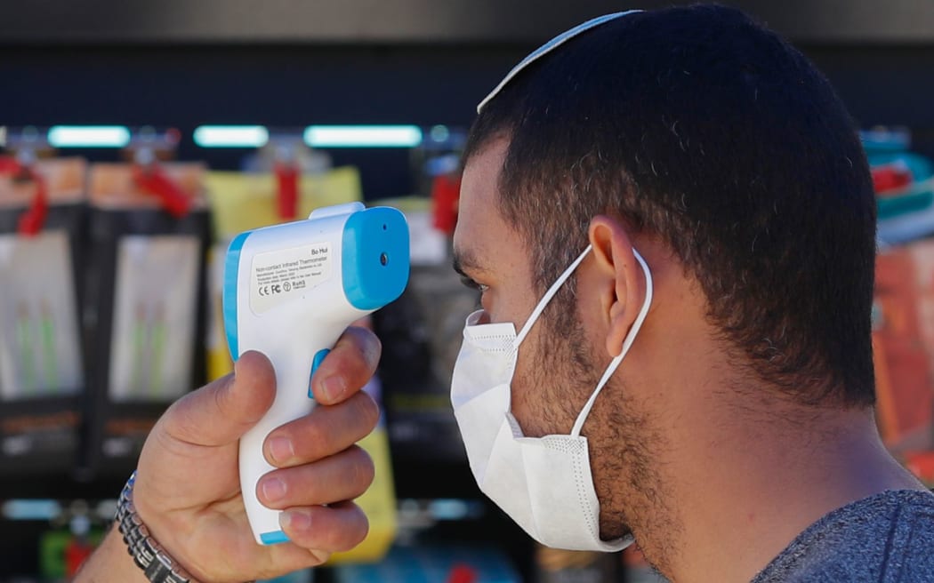 A worker checks the body temperature of a costumer before allowing him to enter the Electro Slil hardware store in Jerusalem during the COVID-19 pandemic, on April 20, 2020.