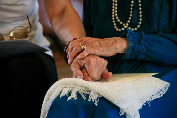 An older woman holds the hand of another person.