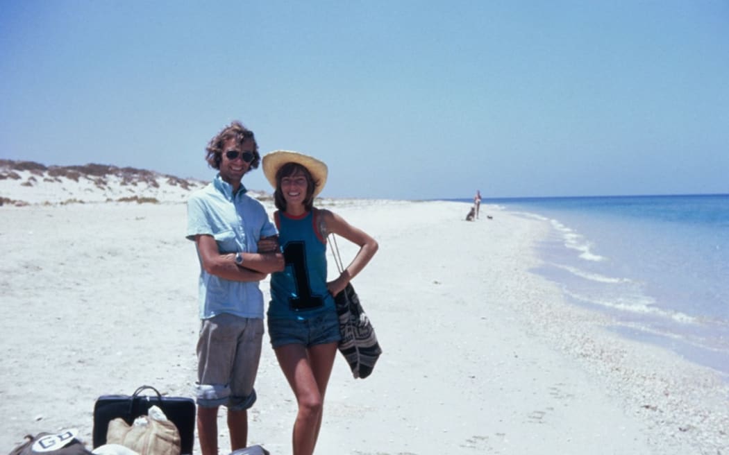 A man and a woman stand on a beach smiling.