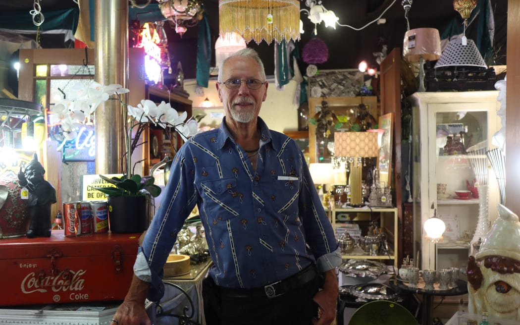 Picture of a man posing in an antique shop, with light shades and artefacts in the background.