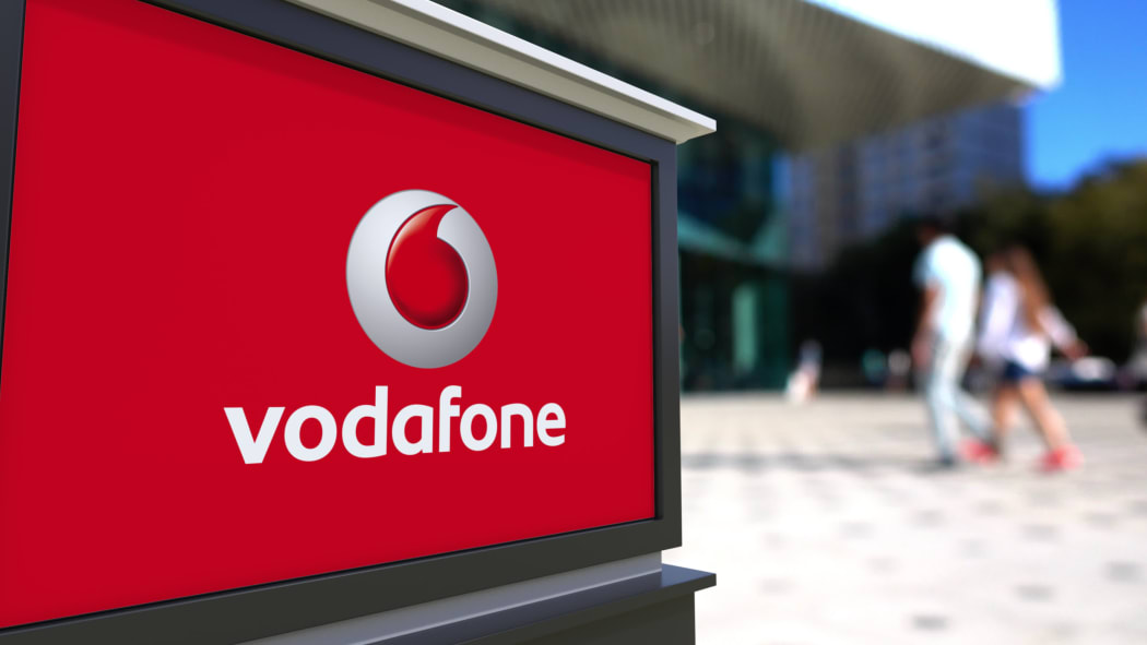 Street signage board with Vodafone logo. Blurred office center and walking people background. Editorial 3D rendering United States