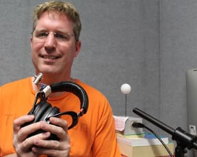 Donald Derrick holds the headphones that are used in the study: the air puff is delivered to the wearer's forehead through the small device attached to the side. The 'ping pong puff air flow meter' is behind him, and is used to measure air flow as people speak into the microphone.