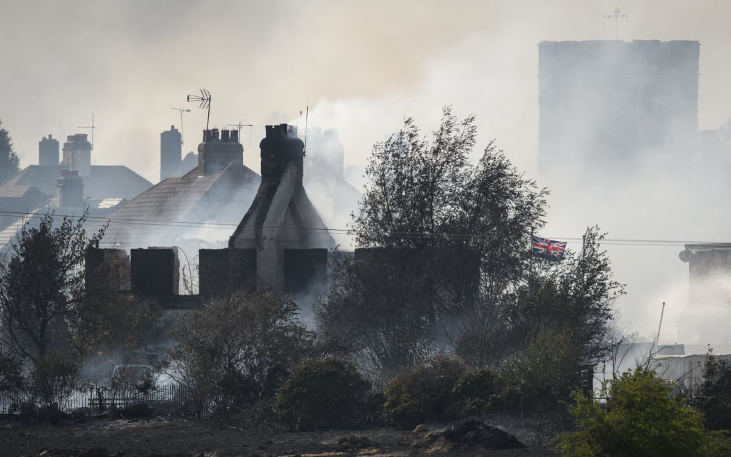 A Union Flag flies amongst the smouldering ruins of houses as fire services tackle a large blaze on 19 July 2022 in Wennington, England. A series of grass fires broke out around the British capital amid an intense heatwave.