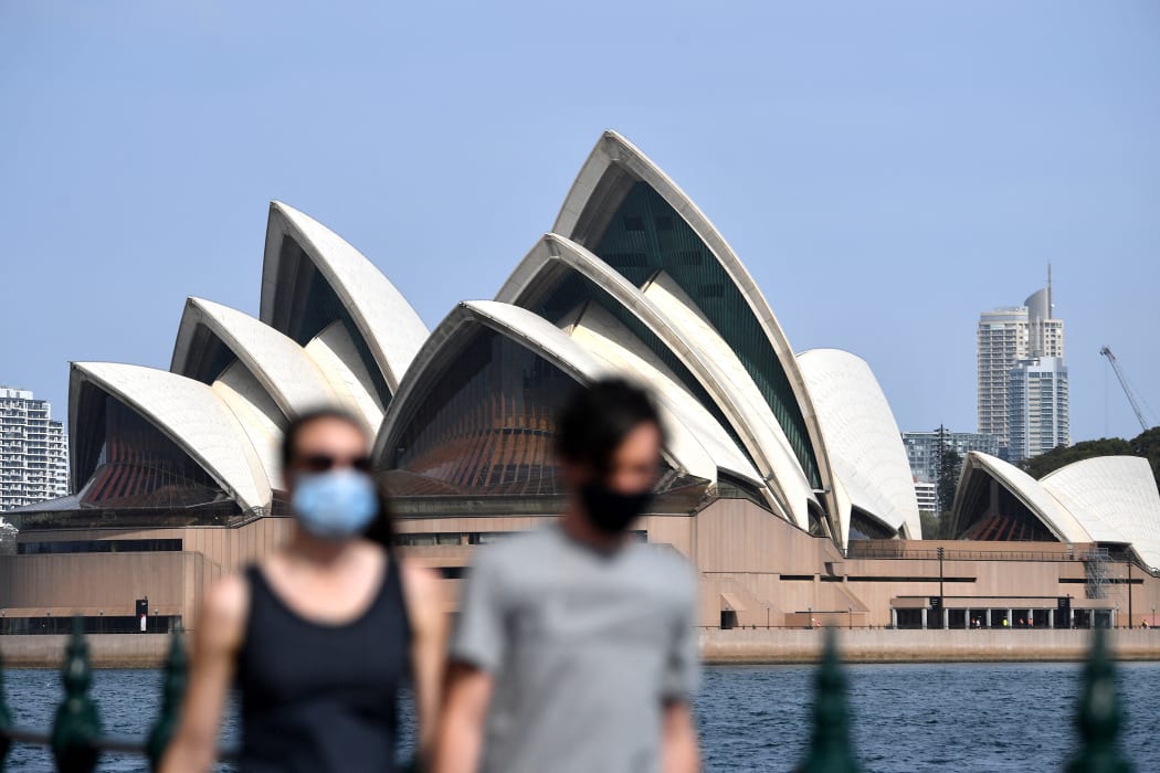 People wearing face masks walk in front of the Opera House in Sydney, New South Wales.