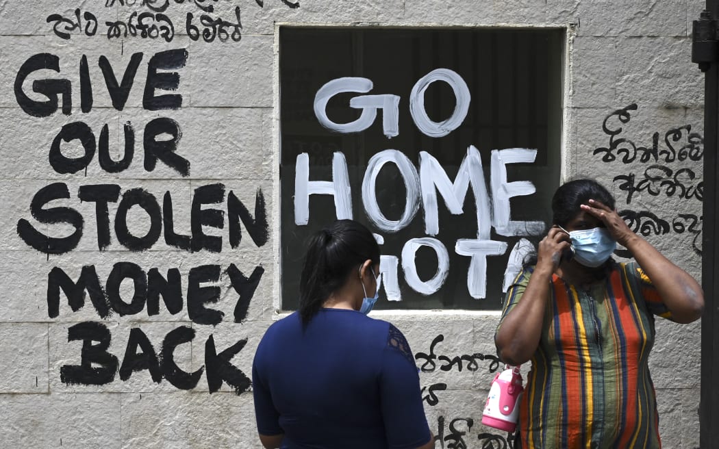 Women stand in front of a graffiti painted outside the premises of Sri Lanka's presidential palace, in Colombo on July 10, 2022, a day after it was overrun by anti-government protestors. - Sri Lanka's colonial-era presidential palace has embodied state authority for more than 200 years, but on July 10 it was the island's new symbol of "people power" after its occupant fled. (Photo by Arun SANKAR / AFP)