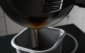 Pouring used cooking oil from frying pan into container, closeup