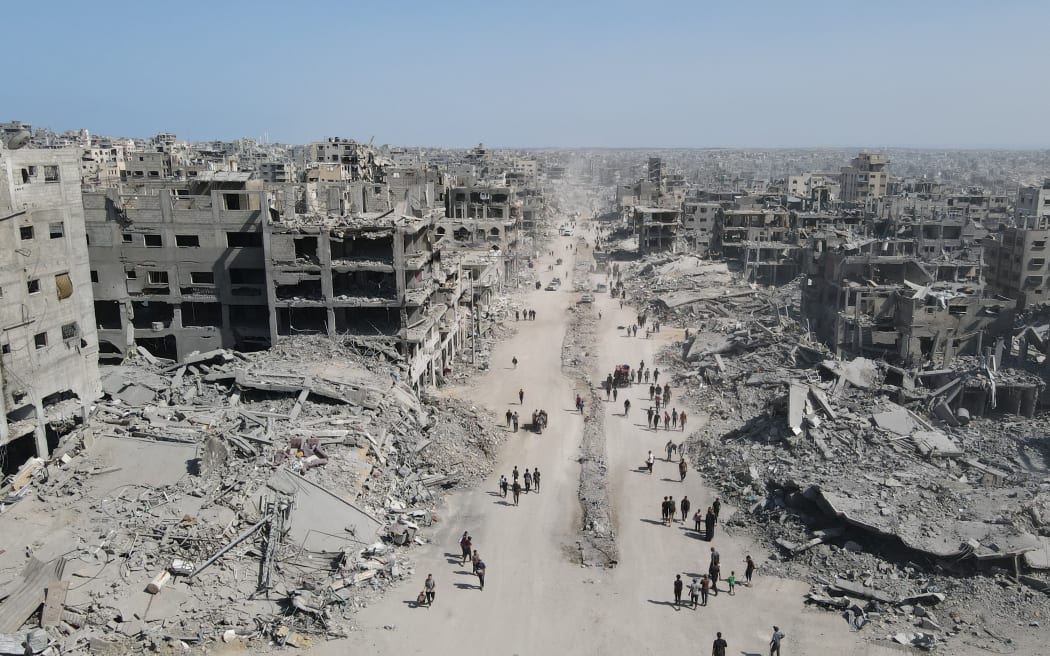 In this aerial view, People walk amid the destruction in Gaza City in the northern Gaza Strip on October 11, 2025, a day after a ceasefire took effect. Israel declared a ceasefire in Gaza and began to pull back its forces on October 10, as tens of thousands of exhausted Palestinians made their way back to their devastated homes. (Photo by AFP)
