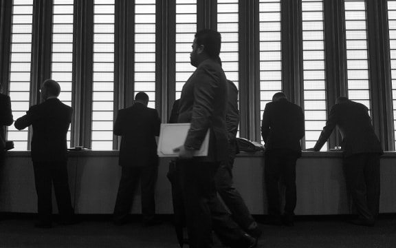 Black and white image of men in suits standing in front of tall window