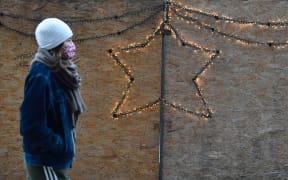 A pedestrian wearing a face mask walks pas passes Christmas illumination on a wooden fence at Alexanderplatz square in Berlin on December 16, 2020, on the first day of a partial lockdown in Germany to curb the number of infections with the new coronavirus Covid-19.