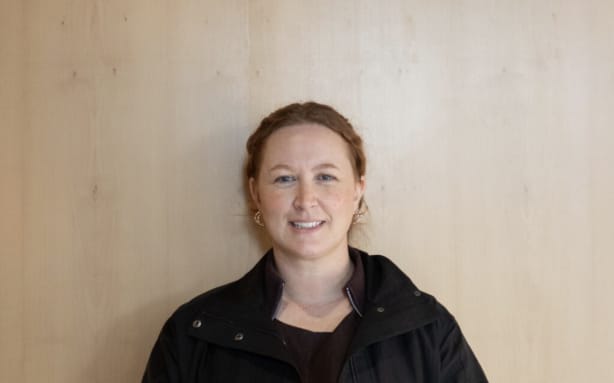 A head and shoulders shot of Kelly Qu, co-owner of MQ Coffee, standing against a wood-grain background, wearing a black jacket.