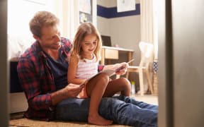 A photo of a father and young daughter reading together