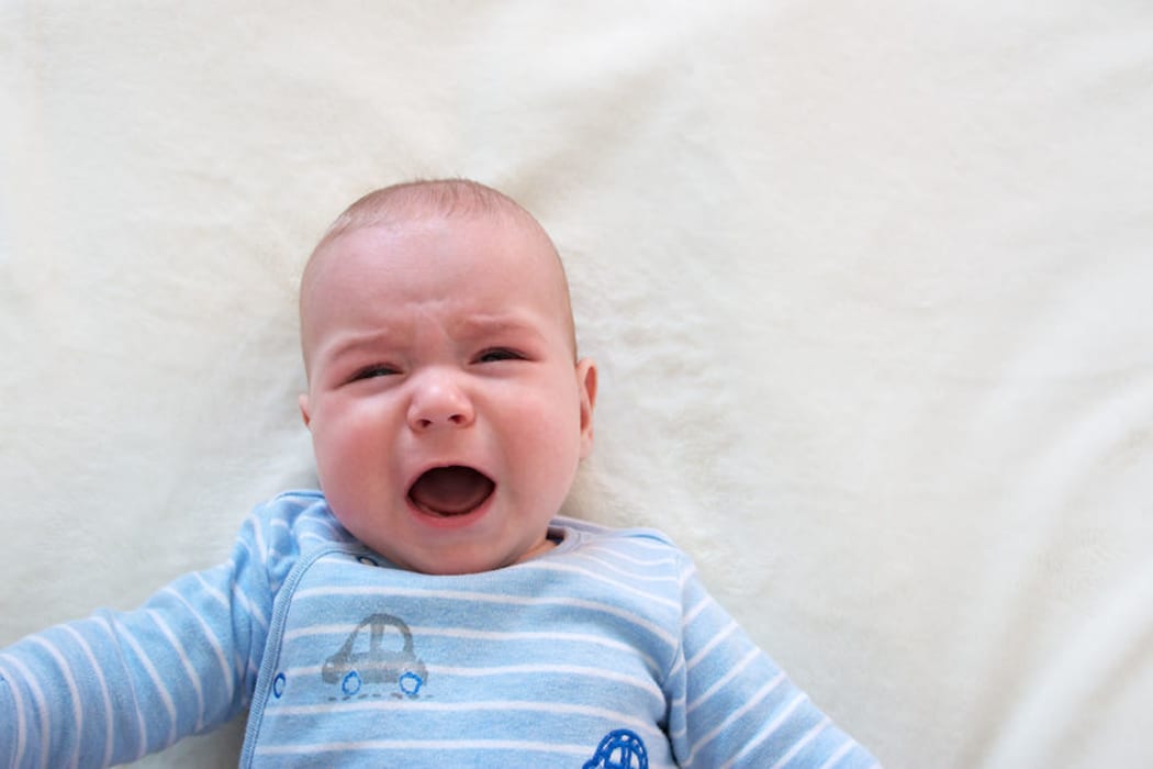 A photo of a little boy crying in his cot
