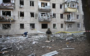 A rescuer works outside a residential building damaged as a result of Russian strikes in Kharkiv on March 27, 2024, amid Russian invasion in Ukraine. In Ukraine's second largest city Kharkiv, which has been reeling from power outages due to the strikes, officials said aerial bombing and shelling killed at least one person and injured 18 others. (Photo by SERGEY BOBOK / AFP)