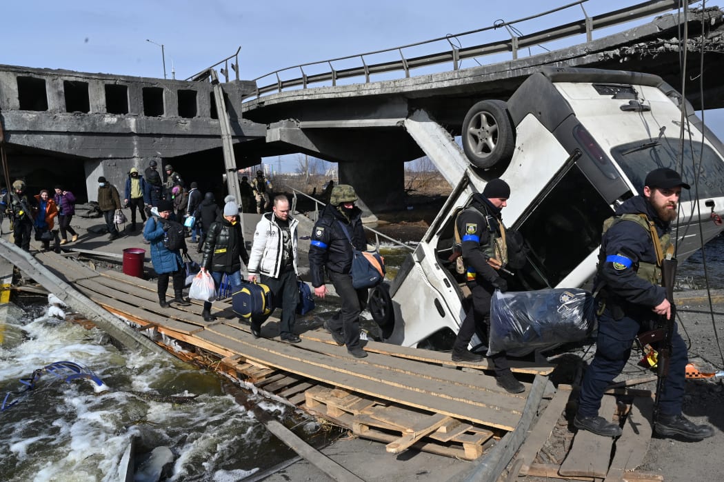 Ukrainian police officers help residents to cross a destroyed bridge as they evacuate Irpin, northwest of Kyiv, on 12 March 2022.
