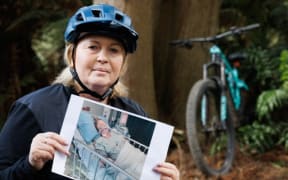 Rotorua woman Kath Cross, in her mountain biking gear in a forest, holds up a printed picture of herself from when she had lung transplant surgery.
