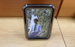 Sincere Standtrue, pictured standing on the edge of a waterfall in his Gloriavale uniform, was placed at the front of the courtroom on the first day of the inquest into his death in 2018.