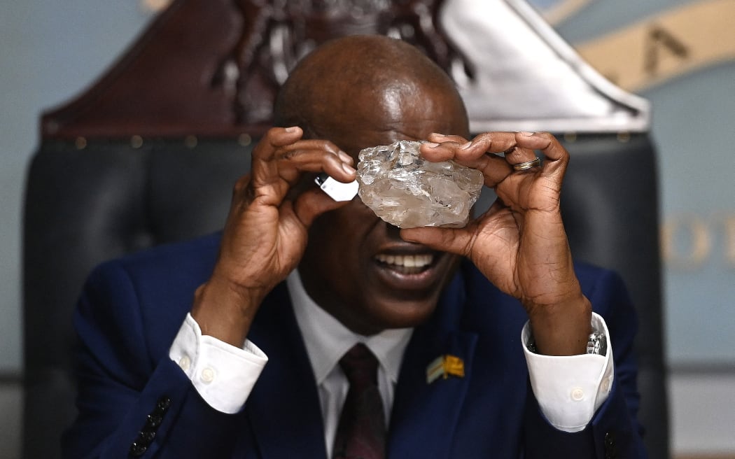 Botswana's President Mokgweetsi Masisi looks at a large diamond discovered in Botswana at his office in Gaborone on August 22, 2024. The 2492 carat diamond was discovered in the Karowe mine in Botswana of Lucara Diamond Company. Botswana is one of the world's largest producers of diamonds, which constitute its main source of income, representing 30% of GDP and 80% of its exports. (Photo by Monirul BHUIYAN / AFP)