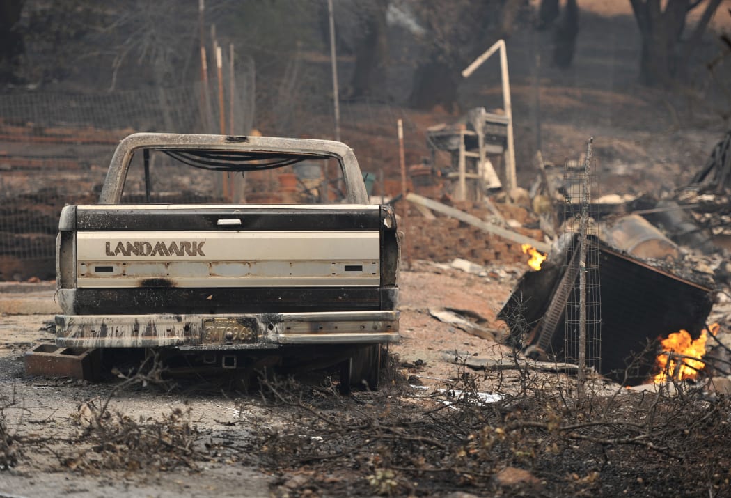 Flames from an open gas line burn next to a destroyed truck in the driveway of a home charred by the Valley fire in Middletown, California