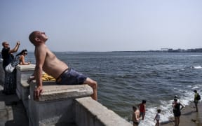 A man sunbathes as others cool off in Tagus River at Ribeira das Naus in Lisbon.
