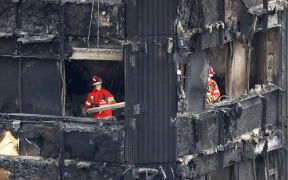 Members of the emergency services work on the middle floors of the charred remains of the Grenfell Tower block.