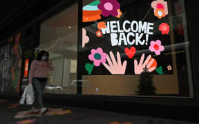 SYDNEY, AUSTRALIA - OCTOBER 12: A woman carrying a shopping bag walks past a ÃWelcome Back!Ã sign in the window of a retail store after stay-at-home orders were lifted across NSW, in Sydney, Australia, Tuesday, October 12, 2021.