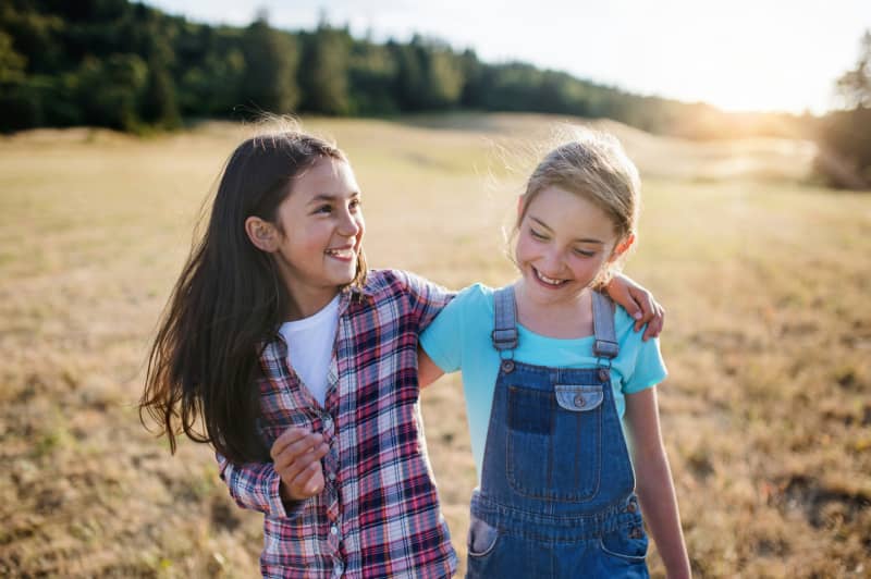 Two young girls with arms around each other, smiling.