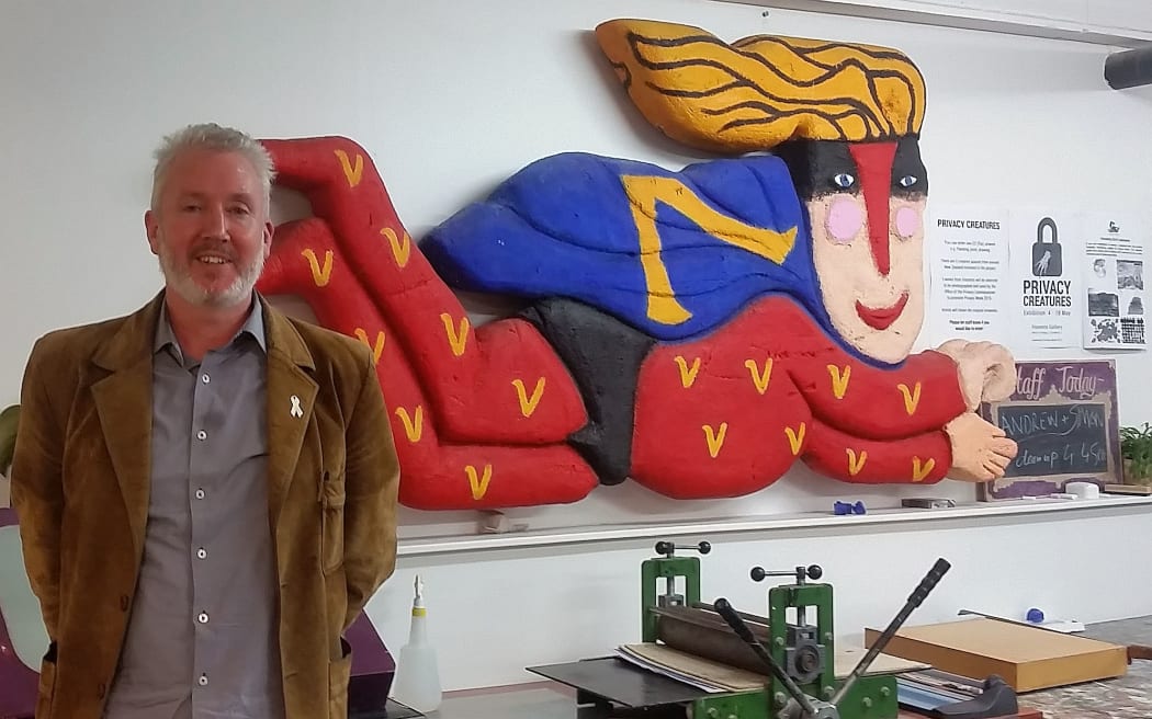 A man with a beard stands in front of a a super character artwork