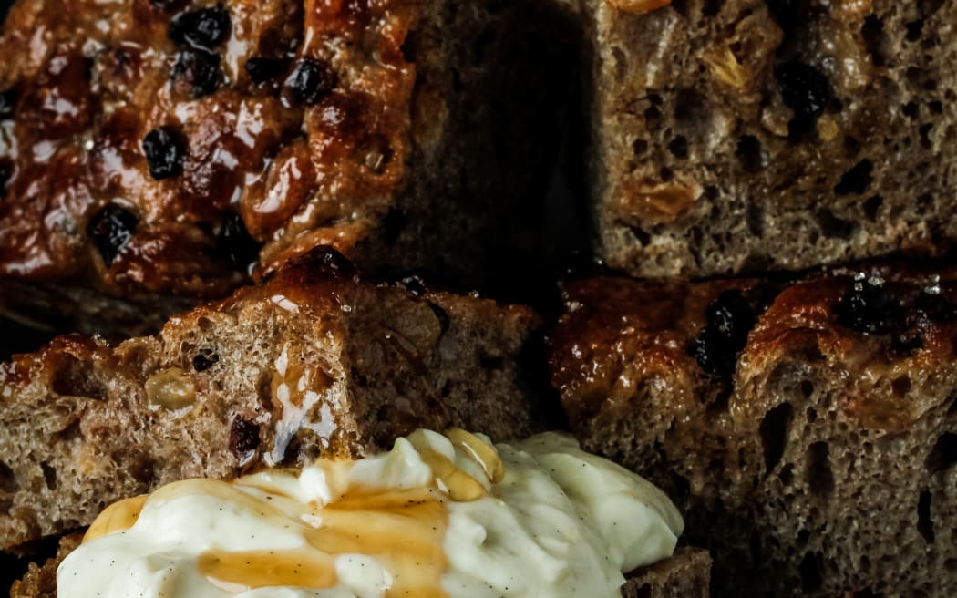 A stack of square pieces of fruit and spice-laden focaccia bread with an accompanying bowl of mascarpone